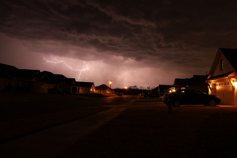Nighttime thunderstorm with lightning illuminating a suburban neighborhood street.